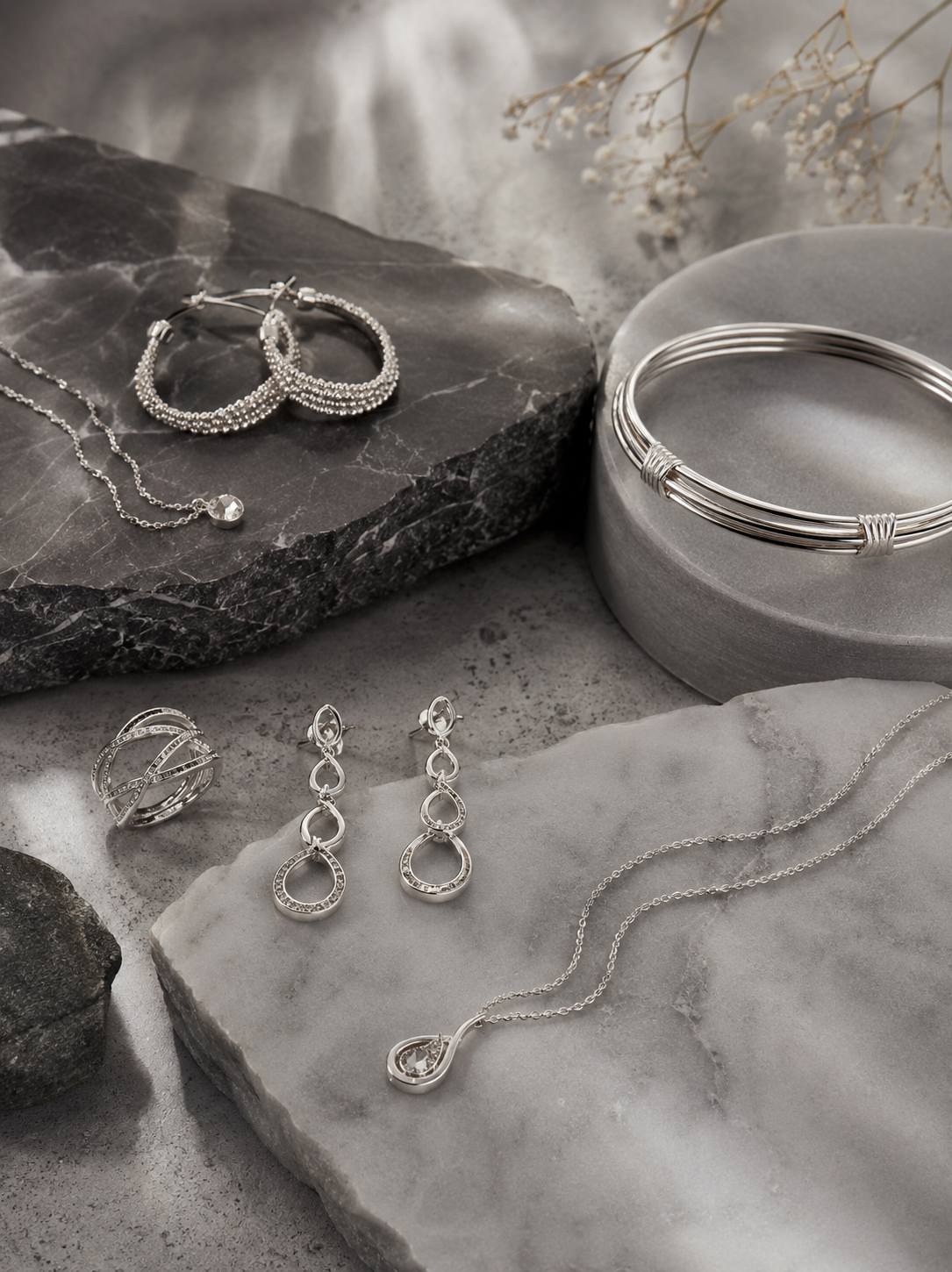 Silver hoops, bangles, rings and pendants styled on grey marble